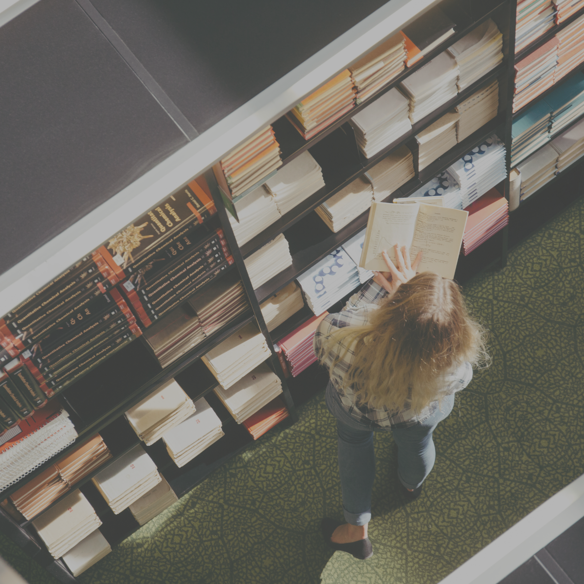 Someone reading a book surrounded by books on shelves. 