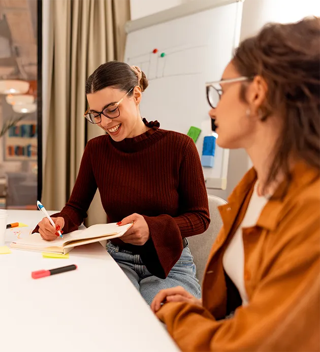 Two young ladies having a discussion with one of them writing in a notebook