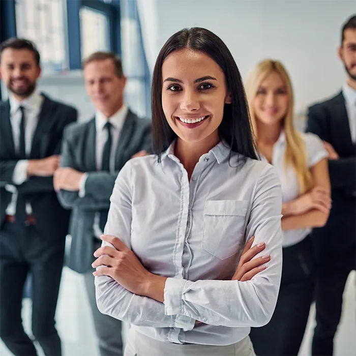 Lady in the foreground dressed in business casual 4 others in the background also dressed professionally in an office environment