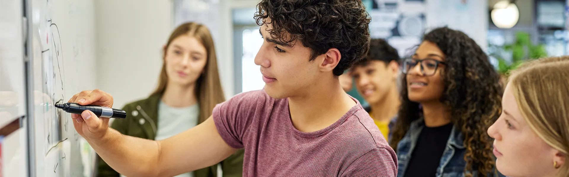 Student writing on a whiteboard with classmates gathered around